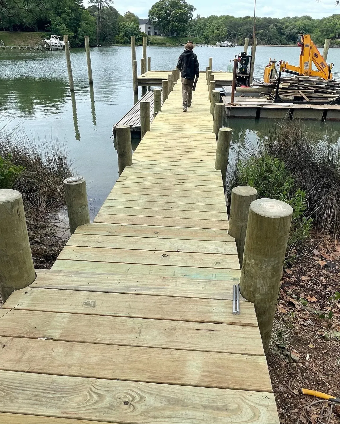 A crew member walking out a new pier, with the barge and excavator at the end