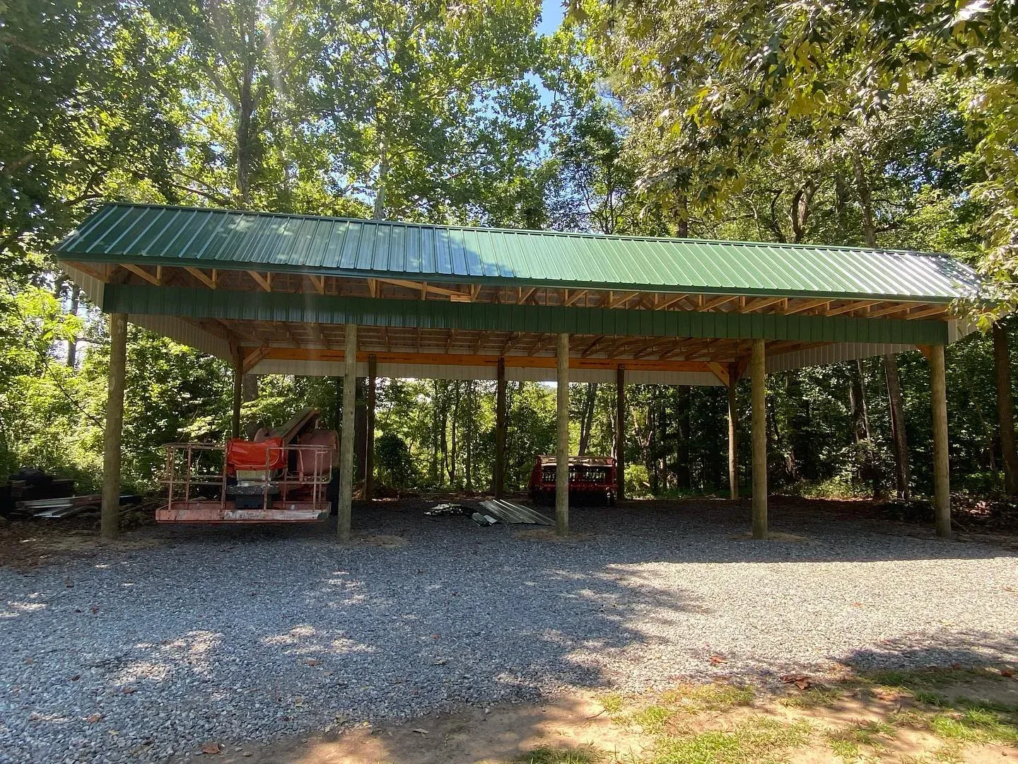 A new open pole barn with a green metal roof over equipment